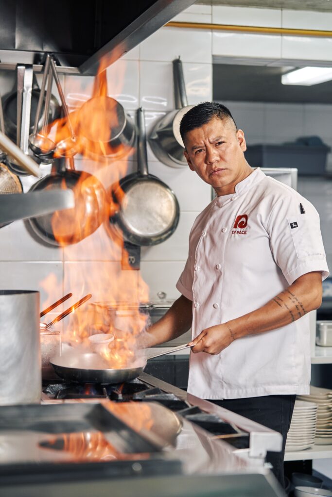 Skilled chef in action with flames in a professional kitchen.